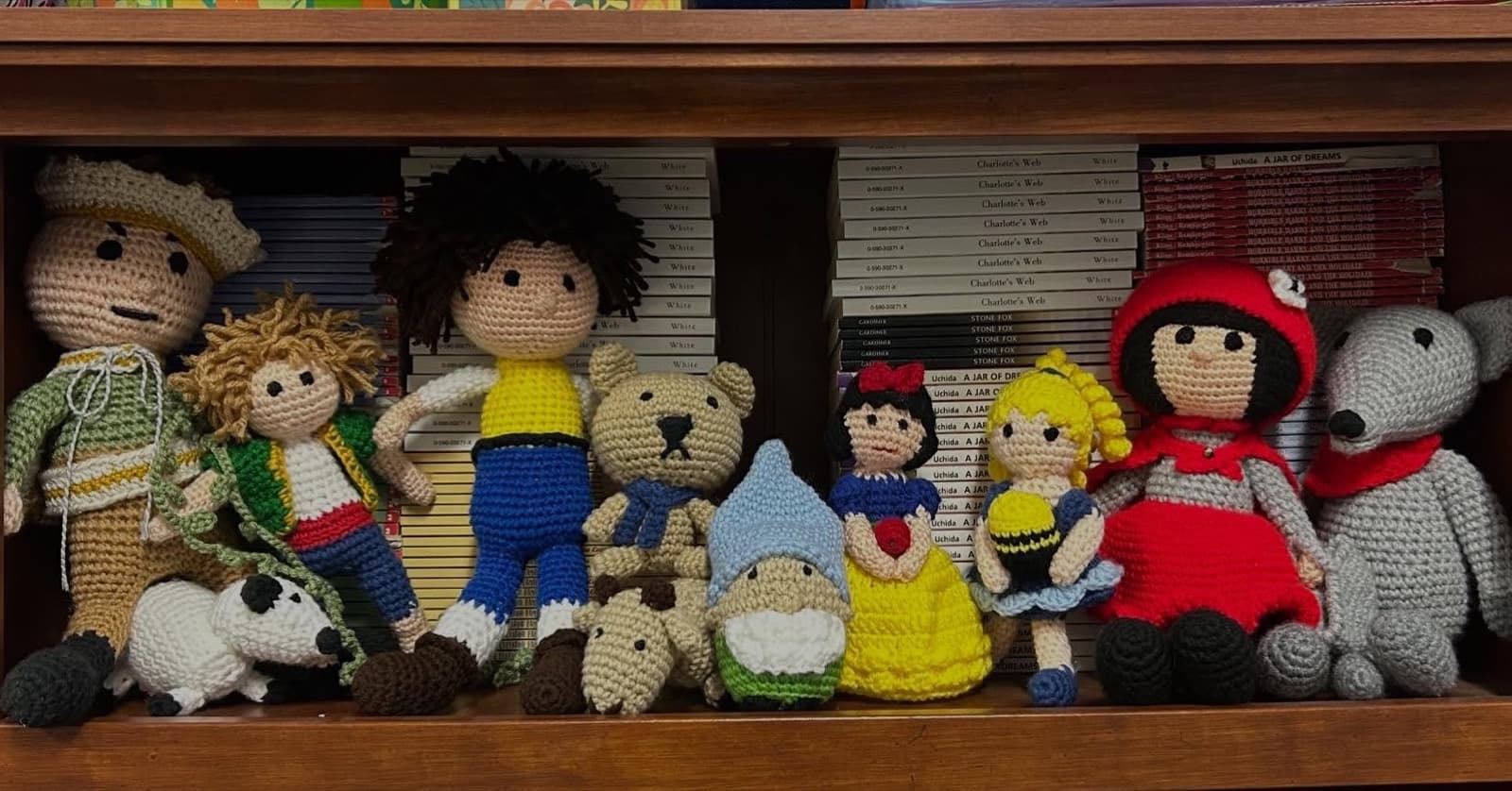 Instagram post: Crocheted dolls of fairy-tale characters, including Snow White and a dwarf, on a bookshelf