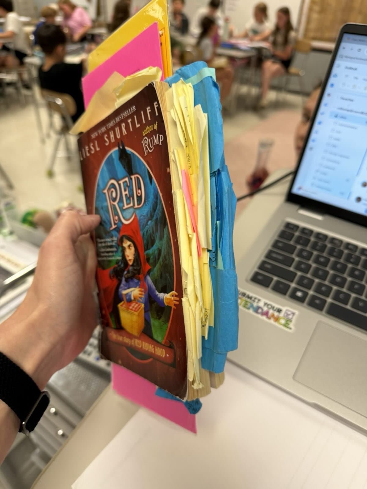 Instagram post: A well-loved copy of RED, stuffed with sticky notes, held up beside a laptop