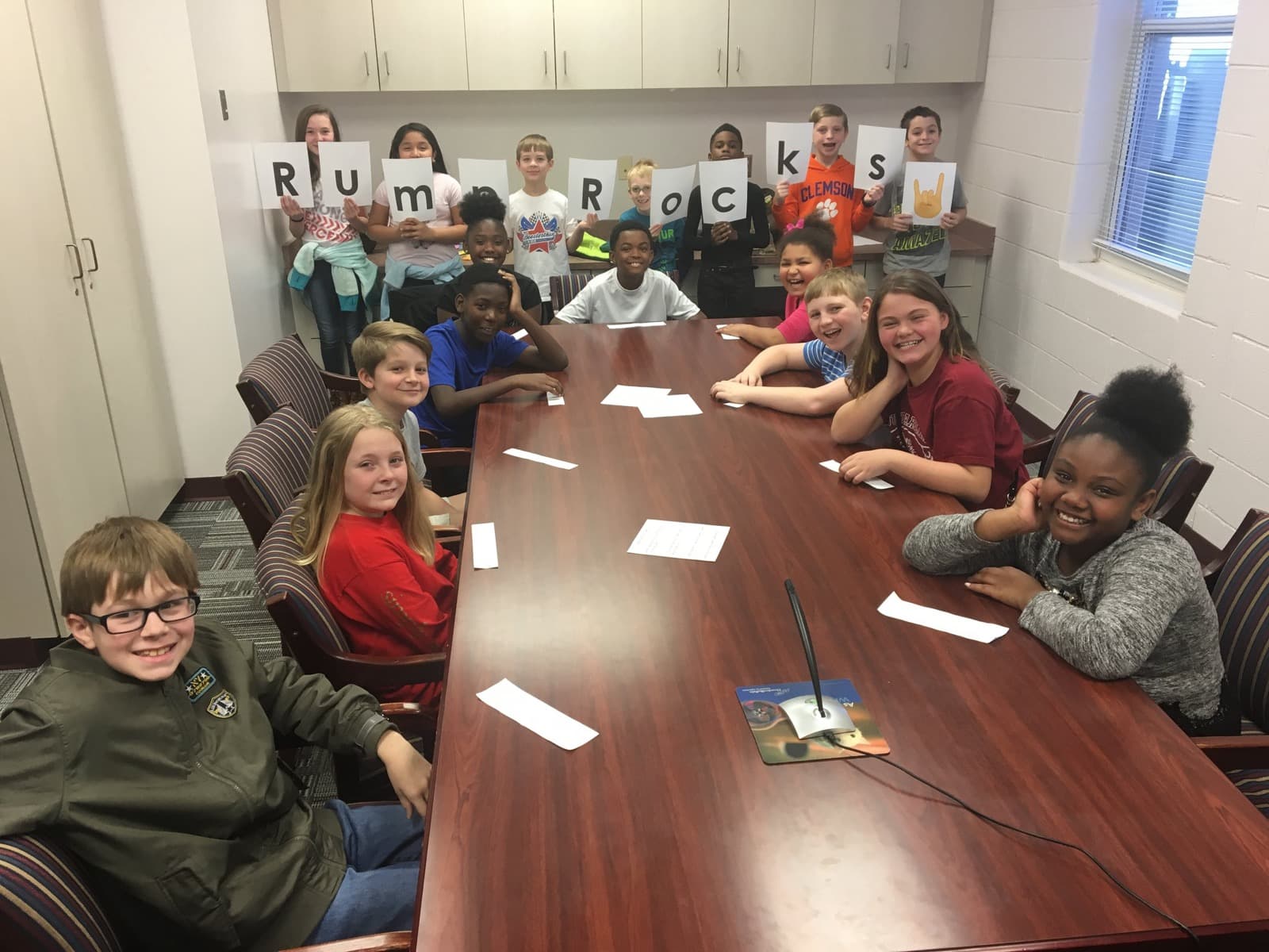 Students around a conference table holding letters that spell “Rump Rocks”
